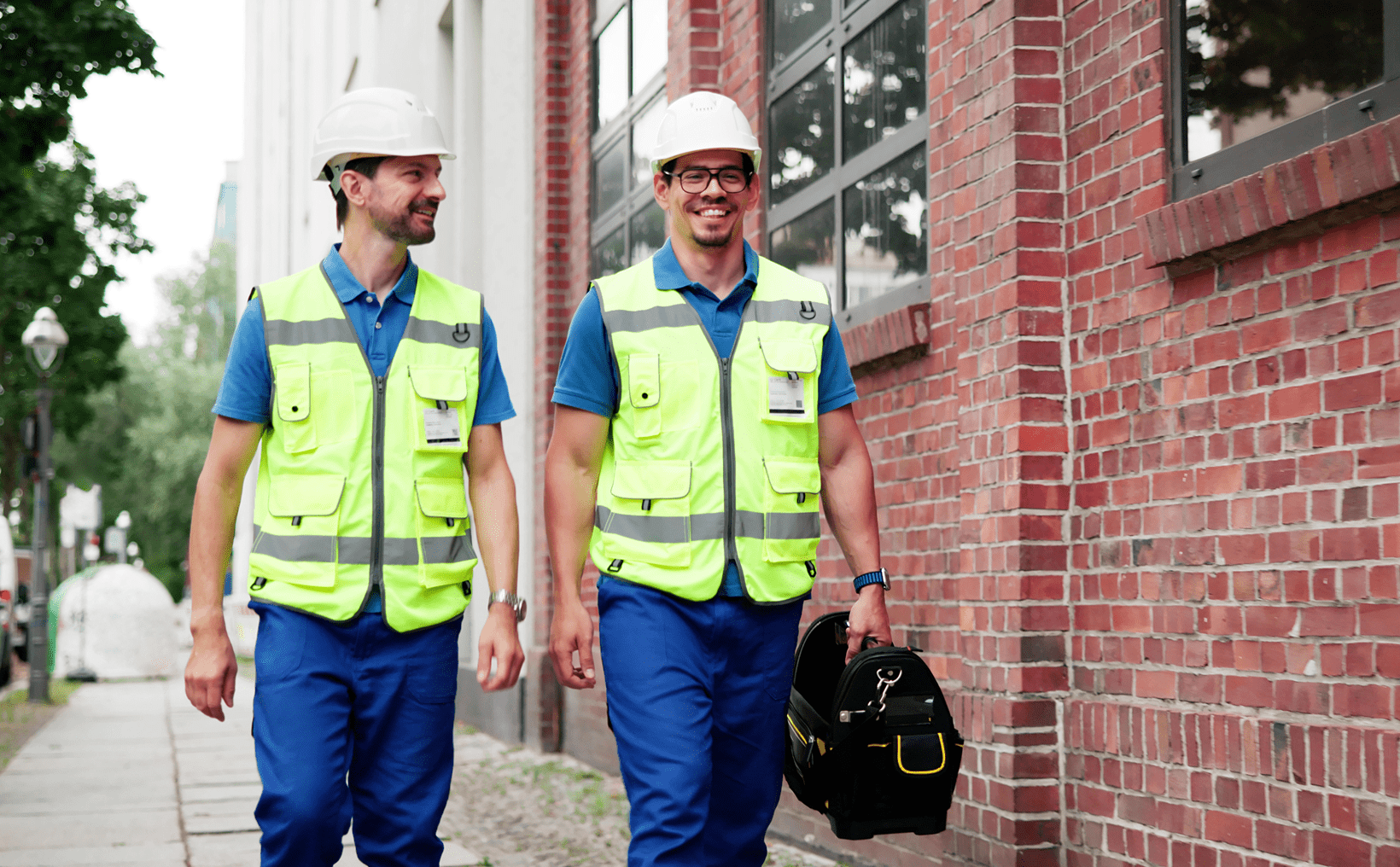 Construction workers walking beside a brick building.