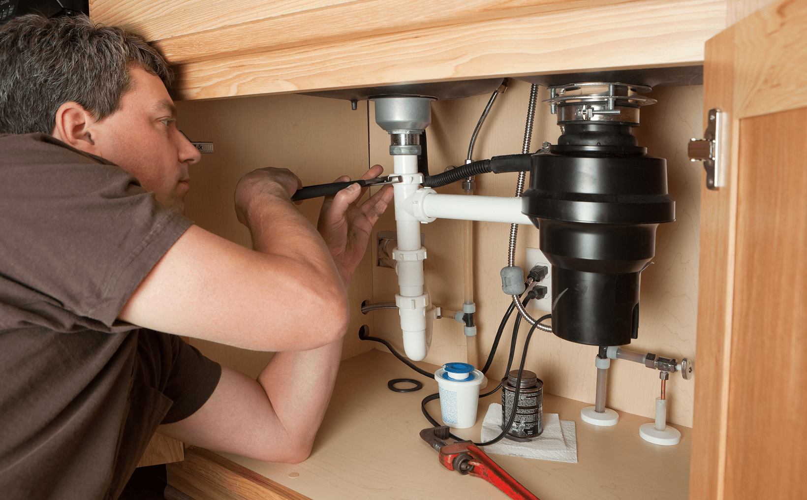 Person fixing kitchen sink plumbing under cabinet.