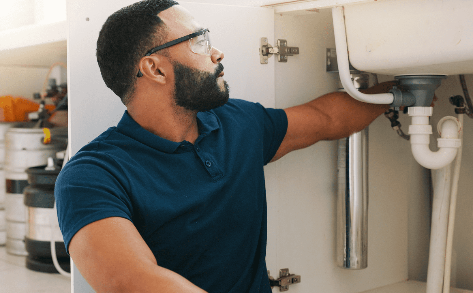 Person inspecting under-sink plumbing pipes.