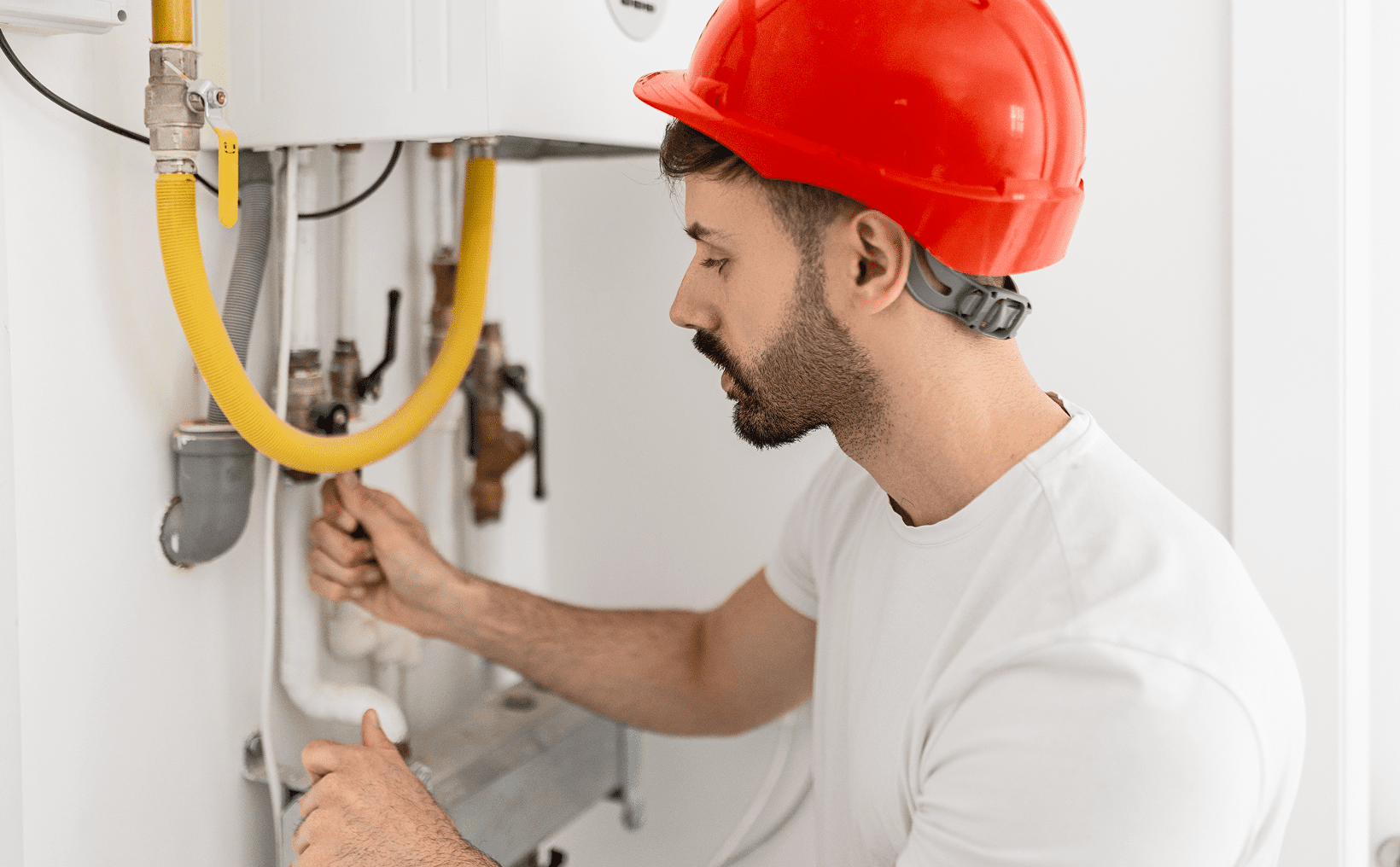 Man inspecting pipes while wearing red helmet.